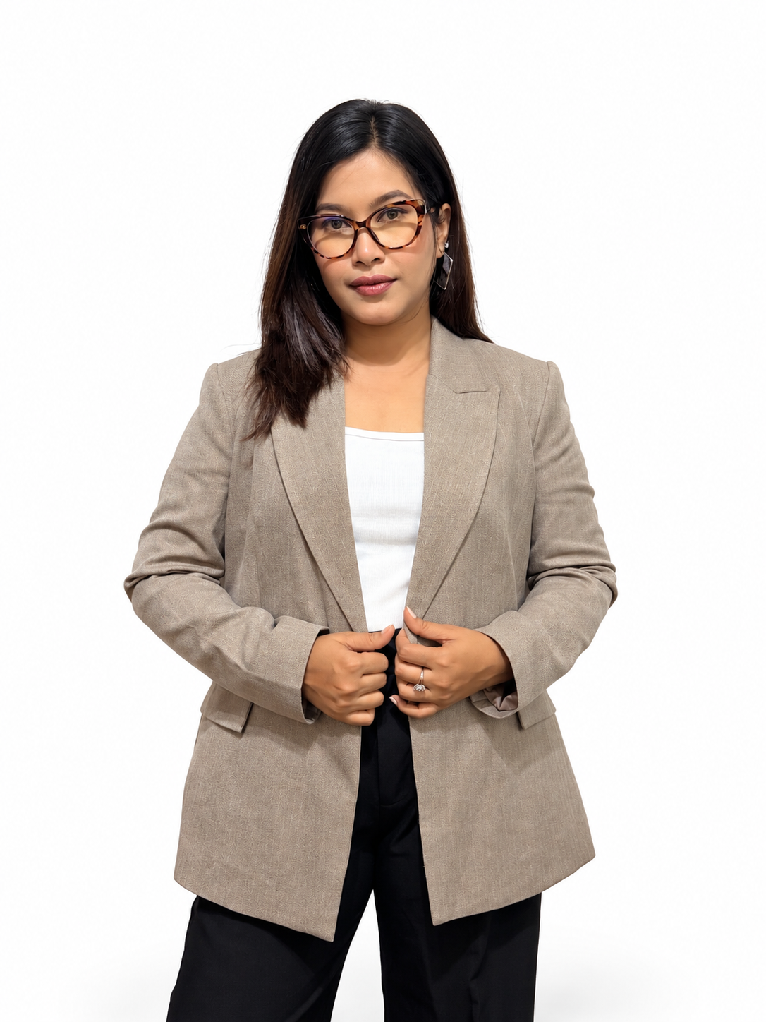 A woman wearing a light taupe-beige blazer over a white top and black pants, standing against a plain white studio background.