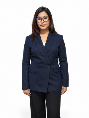 A woman wearing a navy blue double-breasted blazer with black trousers, standing against a plain white background.