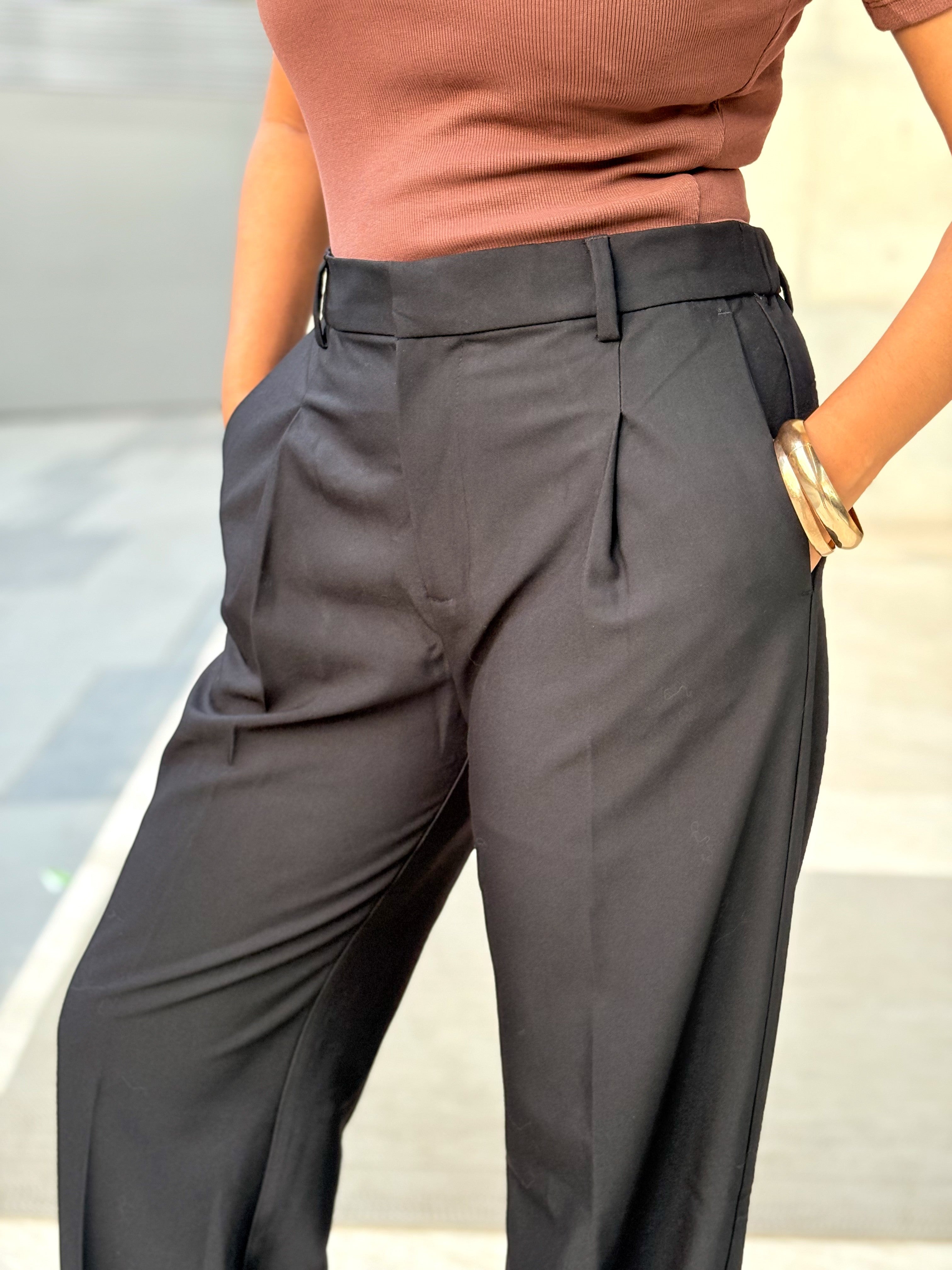 A person wearing high-waisted dark charcoal gray wide-leg trousers with a matching belt, paired with a dusty rose top. The photo is cropped from the chest down, showing the fit and drape of the trousers against a blurred outdoor background.