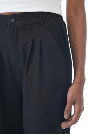 Black pleated pants worn by a person on a white background