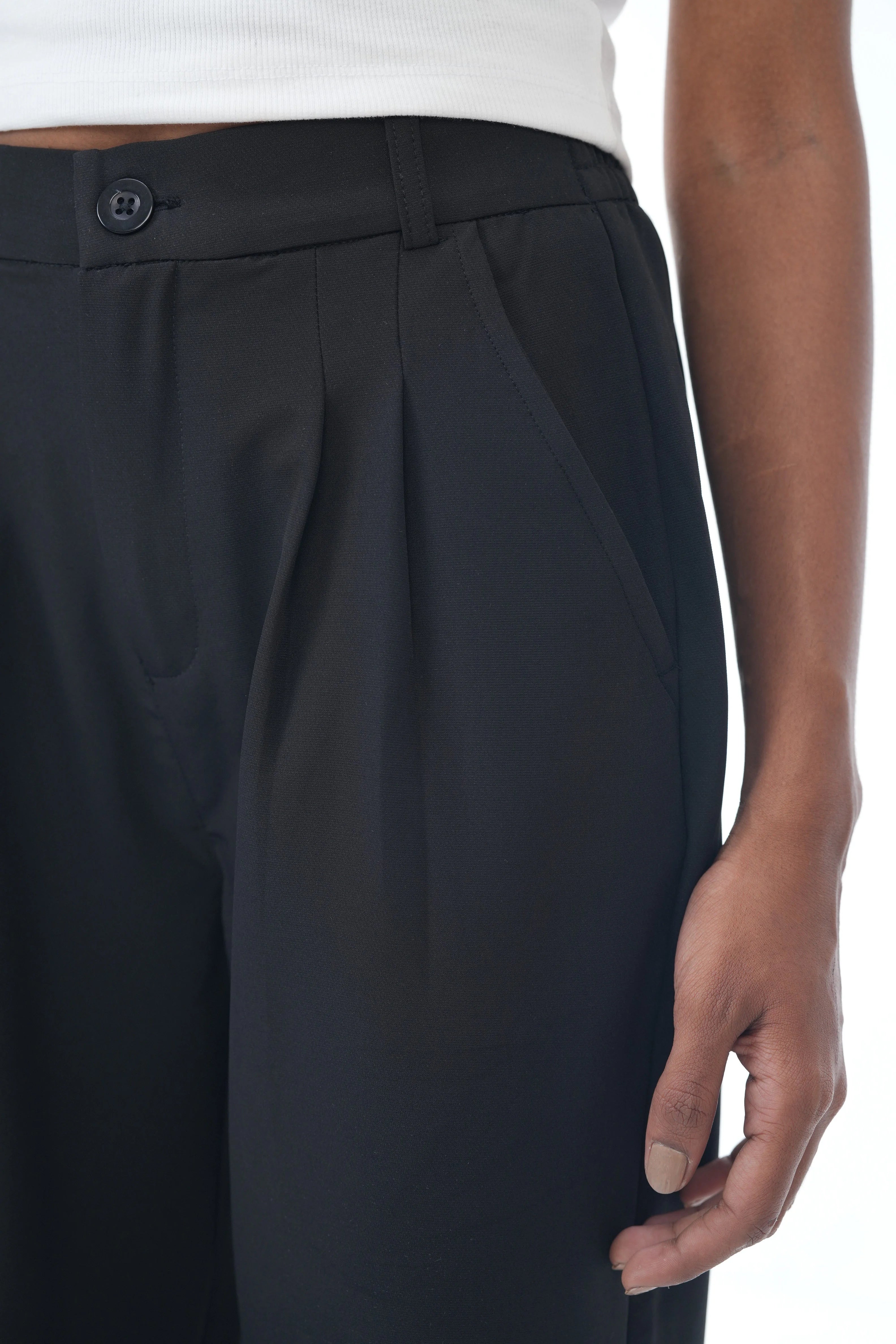 Black pleated pants worn by a person on a white background
