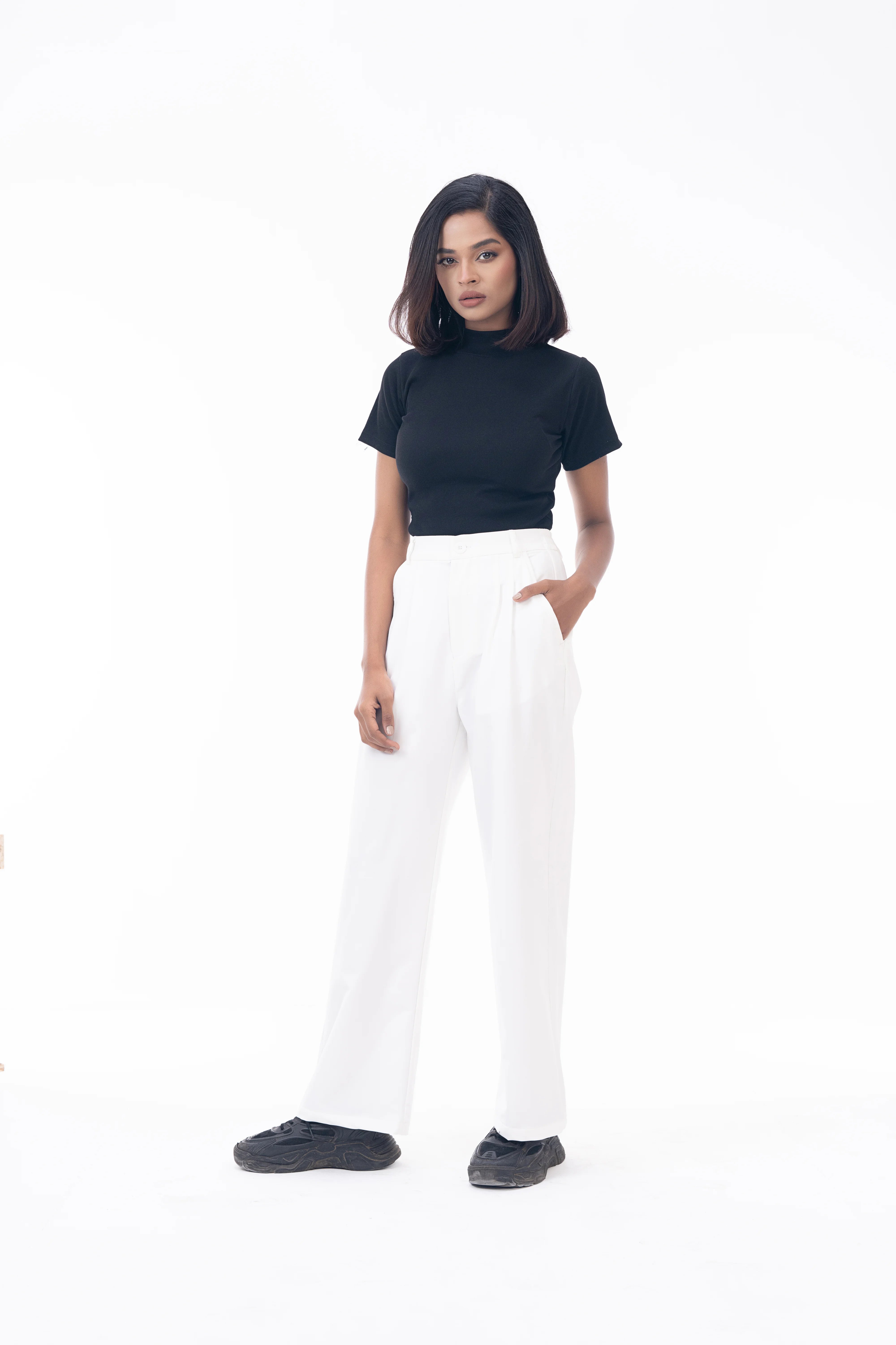 Woman wearing a black turtleneck and white pants on a white background