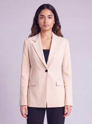 A woman wearing light beige slim-fit formal blazer with notched lapels, front flap pockets, and a single-button closure, styled over a black top and dark trousers. Trendy Buzz BD.