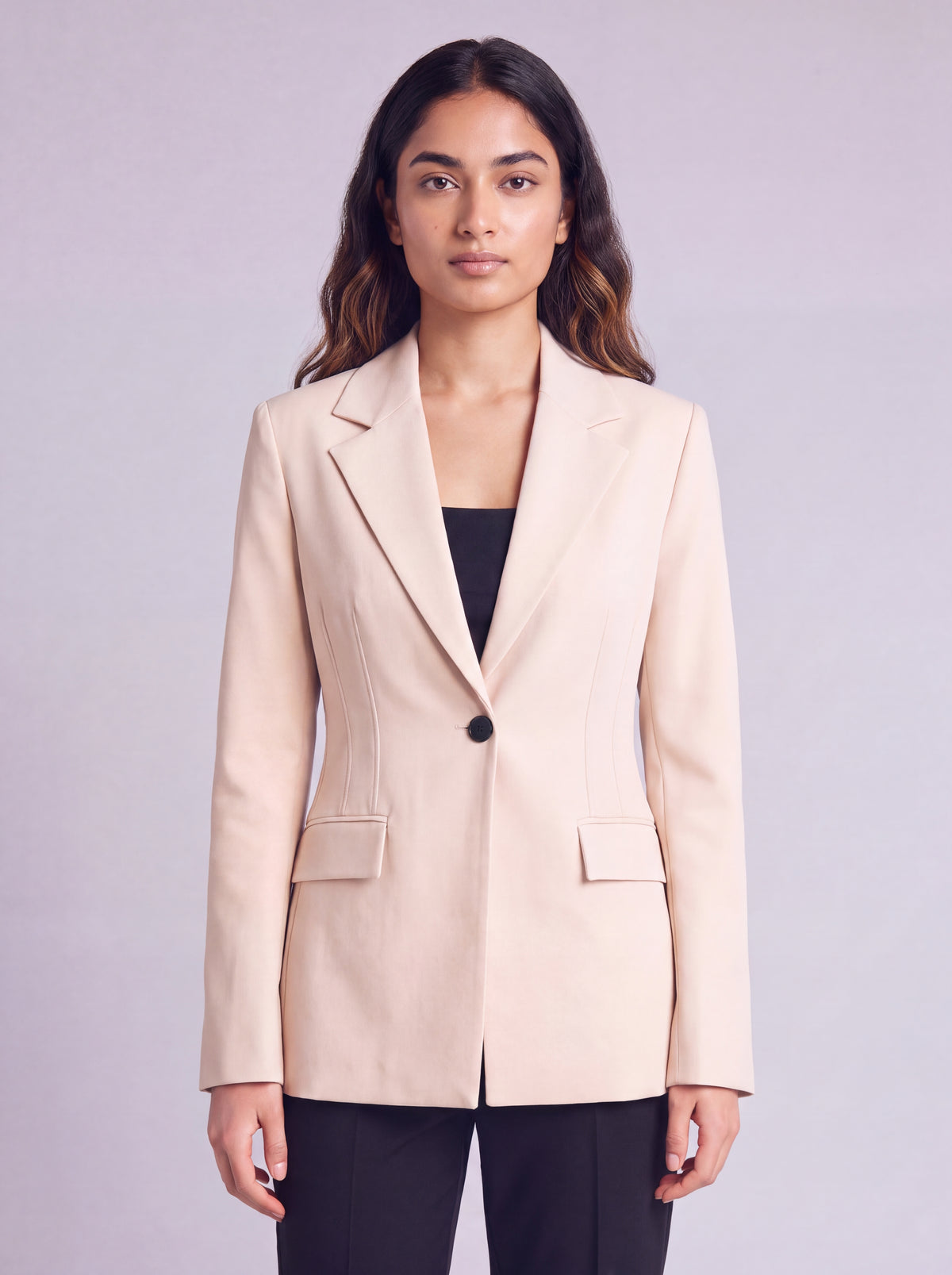 A woman wearing light beige slim-fit formal blazer with notched lapels, front flap pockets, and a single-button closure, styled over a black top and dark trousers. Trendy Buzz BD.
