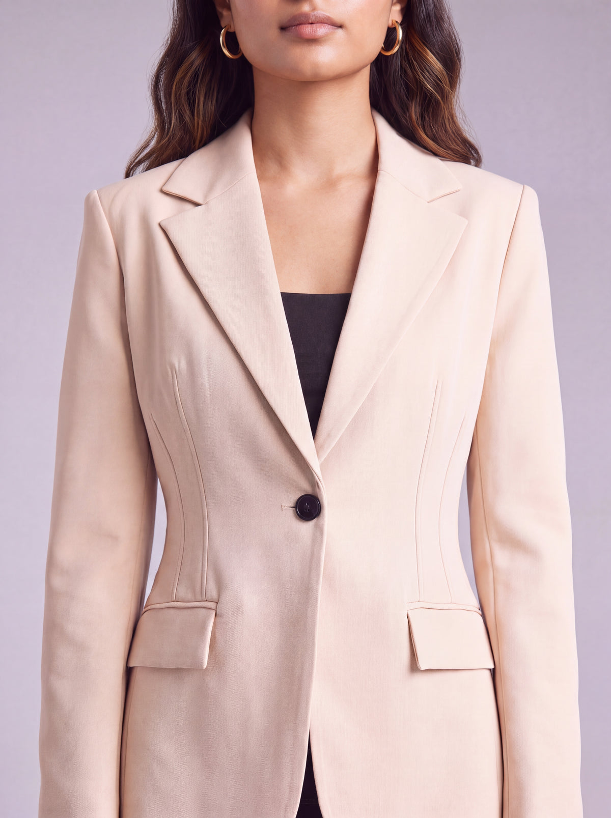 A woman wearing light beige slim-fit formal blazer with notched lapels, front flap pockets, and a single-button closure, styled over a black top and dark trousers. Trendy Buzz BD.