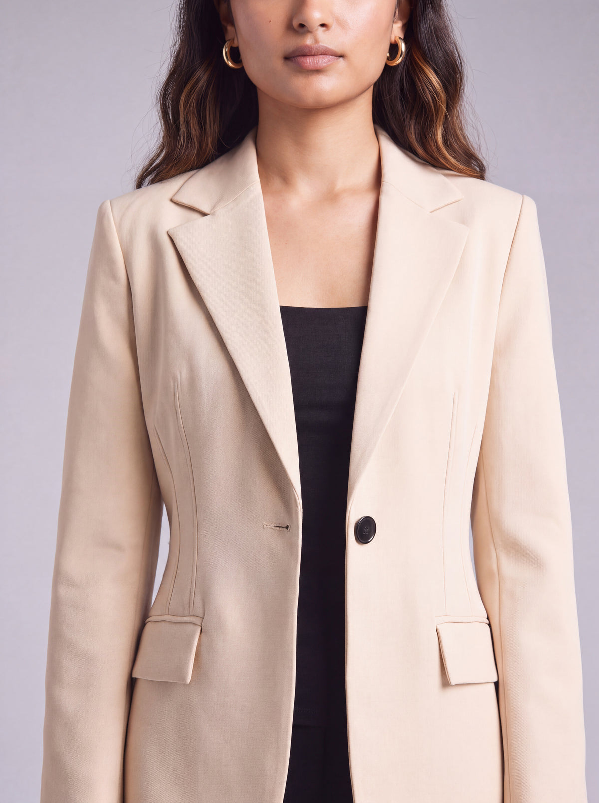A woman wearing light beige slim-fit formal blazer with notched lapels, front flap pockets, and a single-button closure, styled over a black top and dark trousers. Trendy Buzz BD.