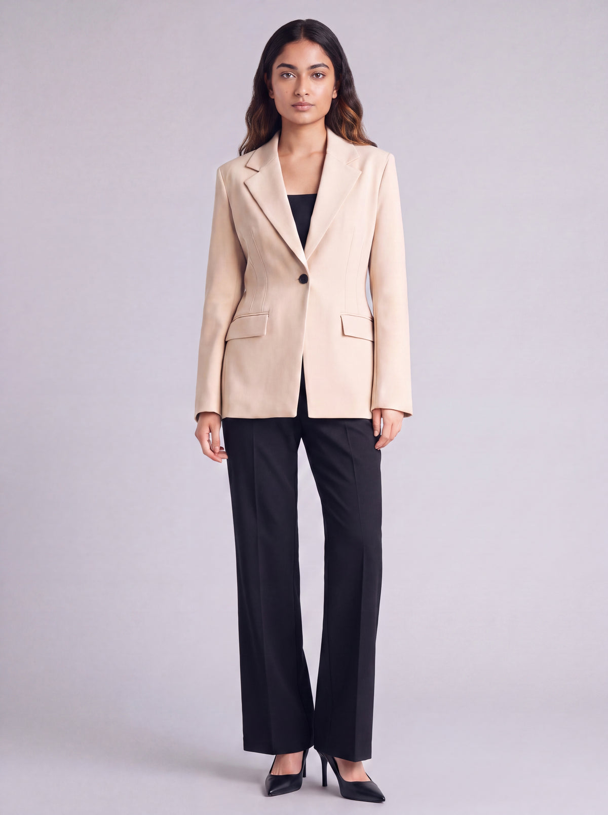 A woman wearing light beige slim-fit formal blazer with notched lapels, front flap pockets, and a single-button closure, styled over a black top and dark trousers. Trendy Buzz BD.