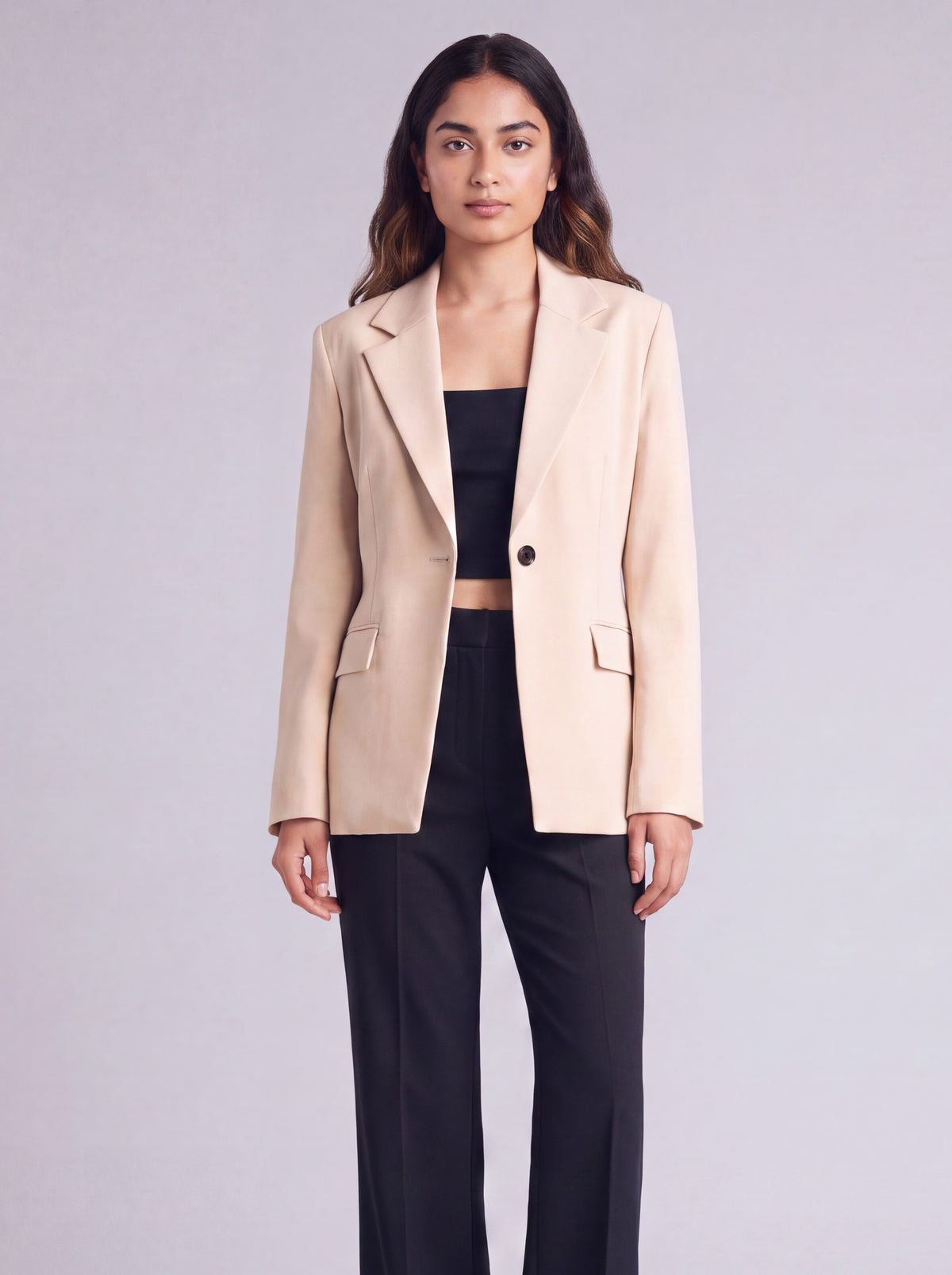 A woman wearing light beige slim-fit formal blazer with notched lapels, front flap pockets, and a single-button closure, styled over a black top and dark trousers. Trendy Buzz BD.