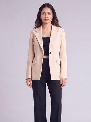 A woman wearing light beige slim-fit formal blazer with notched lapels, front flap pockets, and a single-button closure, styled over a black top and dark trousers. Trendy Buzz BD.