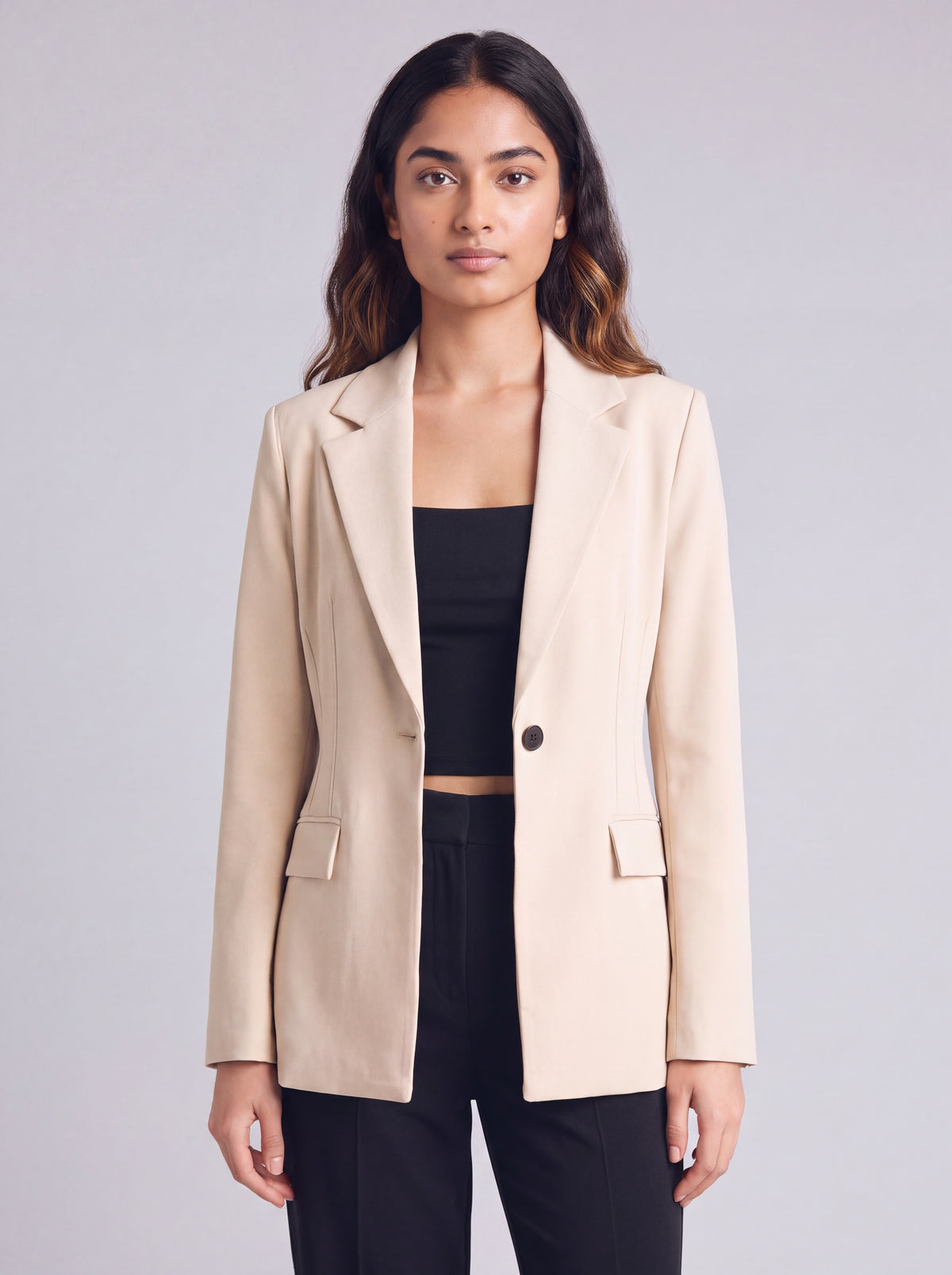 A woman wearing light beige slim-fit formal blazer with notched lapels, front flap pockets, and a single-button closure, styled over a black top and dark trousers. Trendy Buzz BD.